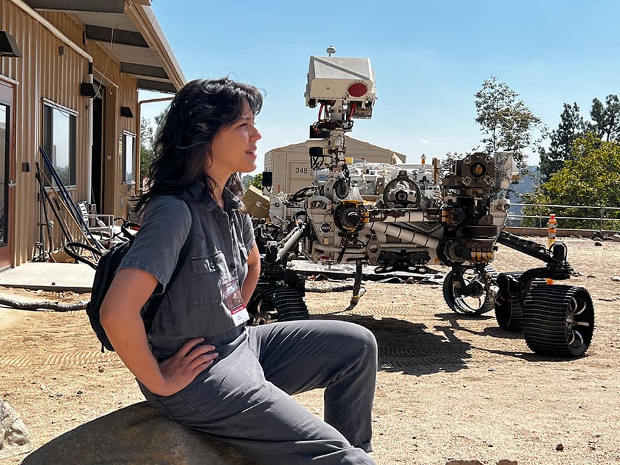 A person looks outward with a planetary rover behind them.