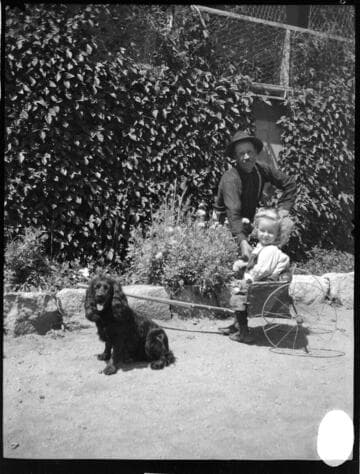 A man playing with a little girl in a cart and a dog