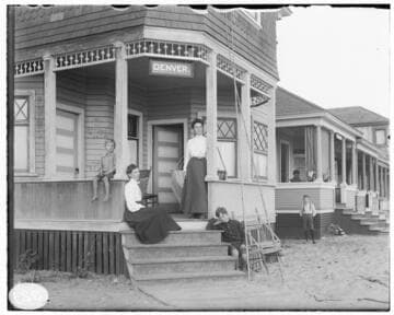 Two women and two young boys on the porch of a beach house with a sign that reads "Denver" over the steps