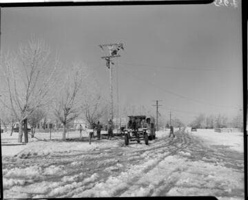 Linemen working on pole in snow at corner of Ave. K