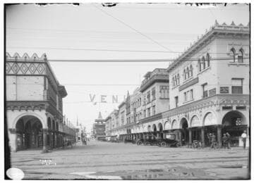 An area view of Windward Avenue in Venice, California, [showing a Turkish Bath House, theaters, an apartment house and automobiles common to 1914 parked along the street.  There is a large sign at the intersection that reads: VENICE.  People are socializing along the street and there is a horse