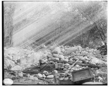 An unidentified scene showing a bed of rocks with trees in the background and small wooden boxes in the foreground