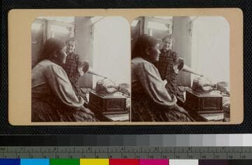 Ramona Lubo speaking into George Wharton James' graphophone, inside his wagon. Behind her is Mary Noble, a teacher at the Soboba Indian School