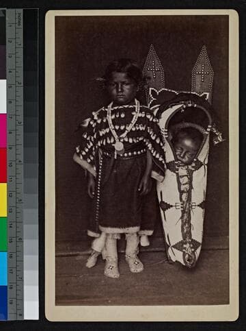 Cheyenne Indian girl standing next to baby in cradleboard