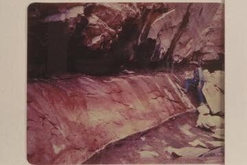 Red stains on rock at spring in Black Water Creek; North side of Navajo Mountain.  Black Water Cave.  Tom Daly in the background