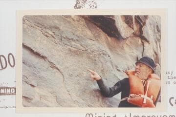 Dock Marston posed at the D. Julien inscription at Mile 185.75, Cataract Canyon.  A later Visiting group pictured an 1891 inscription to the right of the D. Julien and a part would be aboVe the pointing arm