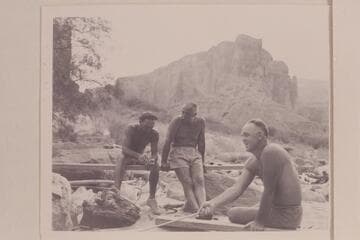 Moulty Fulmer toasting bread at Nancoweap Camp. Other figures are Nevills and Masland