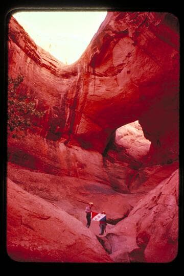 Masland and Marston holding Explorers Club flag at natural bridge in Navajo Canyon. Masland proposes name, "Ba-Sah Bridge," for the seven pot-holes below it
