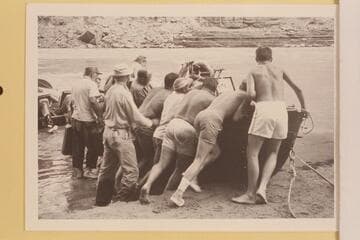 The Marston-Disney crew rolling a boat at Mile 166. Doc Reed holds the jeep cans. Jim Algar can find no room to get in. Russ Haverick, Garth Marston and Les Gear are in there pitching. Buzz Belknap lacks leverage