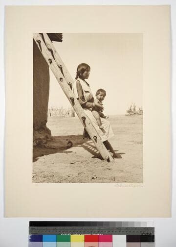 Zuni woman with baby in her lap, leaning against a wood ladder