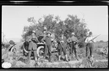 Five unknown men wearing suits and ties in the field with shotguns on an hunting trip