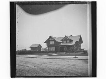 Unidentified two-story house with large lawn and new trees, street view