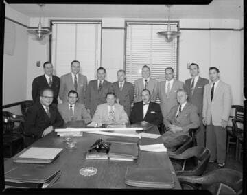 Board room with men in suits around posed around a table