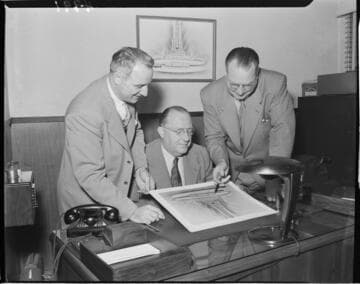 Three men at desk reviewing an archetect's rendering of a new "McDonalds Famous Hamburgers" building