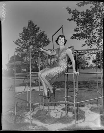Young lady in a dress and high heals sitting in monkey bars at park playground