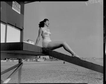 Woman in bathing suit sitting on lifeguard tower ramp at the beach