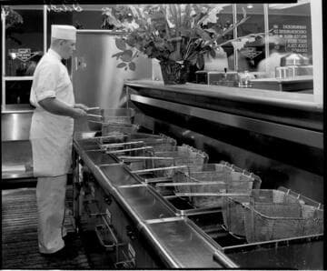 Cook working at a long row of deep fat fryers in a fast food restaurant
