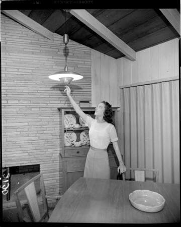 Lady pulling down retractable lamp over table in dining room