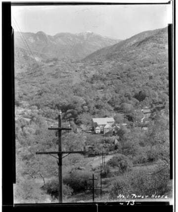 View of Kaweah #1 Power House on a hill with transmission towers in the foreground and mountains in the background