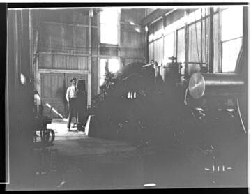 An operator is standing by one of the water turbines in the interior of Kaweah #2 Power House