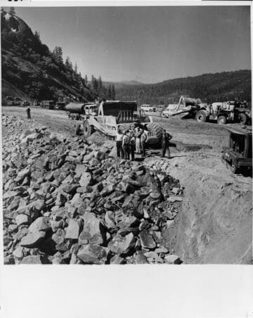 A long procession of earth-moving equipment carried on the process of building the earth-fill dam across the San Joaquin River