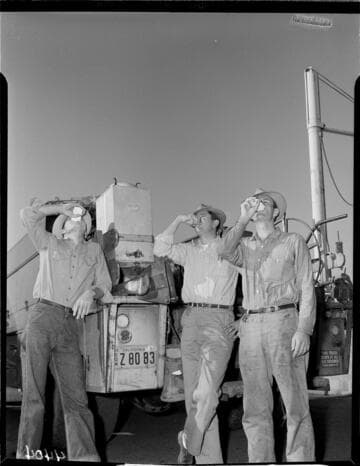 Three linemen drinking water from jug on back of line truck