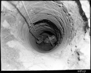 Man in hard hat looking up from the bottom of a narrow hole in the ground