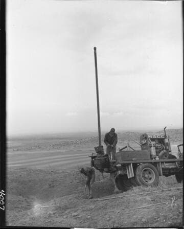 Men using power auger rig on truck to dig hole for pole placement