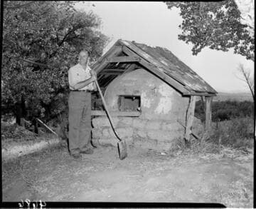 Man holding a shovel standing by a large, domed, clay, oven