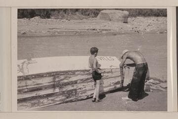 Norm Nevills repairing boat (?) after hitting rock; probably Nokai (?) Rapids.  Jackie Frost watches