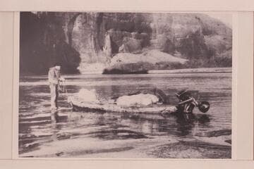 John Wetherill on the icy shore of Glen Canyon holding the painter of the outboard skiff used in a trip up to Rainbow Bridge and Hole in the Rock