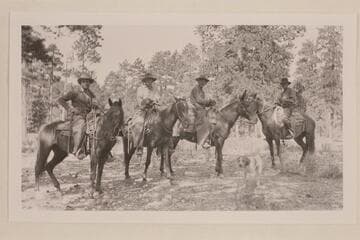 Uncle Jim Owen on mule. Ammon Davis at right. The dog in foreground was the leader of Jim's pack. A brass plate on his collar was inscribed: My name is Pot Hound. I have been at the death of 155 lions