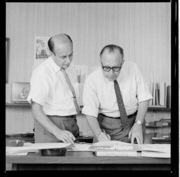 Engineer and draftsman reviewing layouts in the drafting department and manager's office