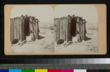Hualapai Indian woman in doorway of house. A large basket is at the left