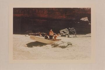 George Wing hung on a rock with one of the Nevills San Juan punts near Johns Canyon. In the punt are Susie Reilly; Wing; Smith; Pat Reilly. Mexican Hat gauge: 1190 cfs