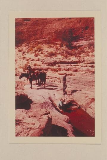 Water hole in Bald Rock Canyon. Tom Daly crouches by the water. Tobe Owl stands above him. Christy Turner is on the horse