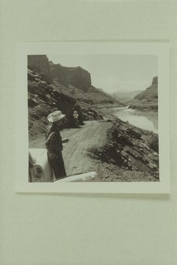 Down the Colorado River toward Castle Valley. The Fisher Towers in distance. George White stands by the car while Russ Haverick takes photos of the possible location for a Powell picture scene