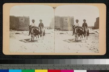 Two Pueblo Indian men on horses, with stone building in background